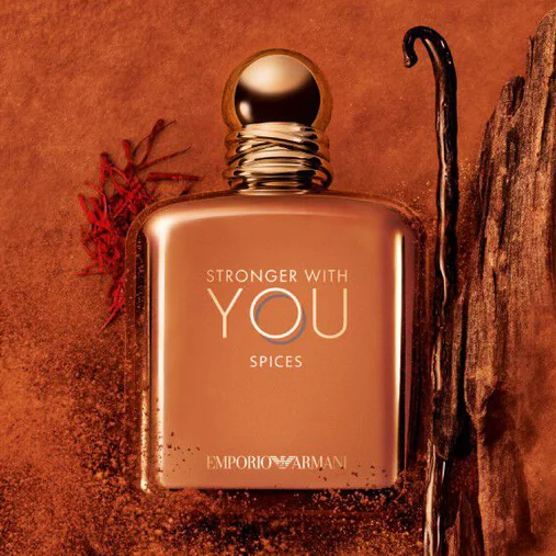 ARMANI STRONGER WITH YOU SPICES bottle with gold cap, placed among vanilla beans and saffron on an orange textured background, highlighting the fragrance’s spicy, gourmand notes.
