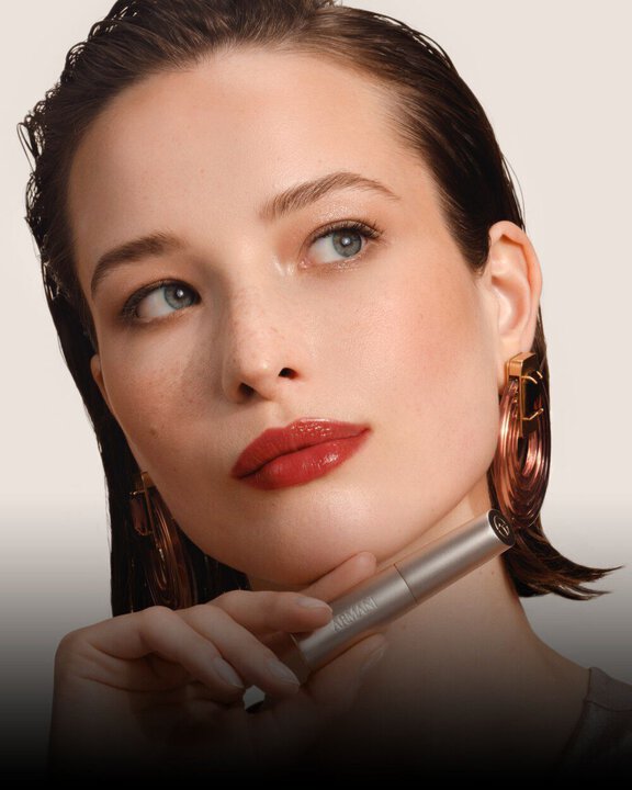 Armani Prisma Flash Scarlet Flash lipstick, showcased during application, emphasizing its bold, vibrant red pigment and sleek tube.