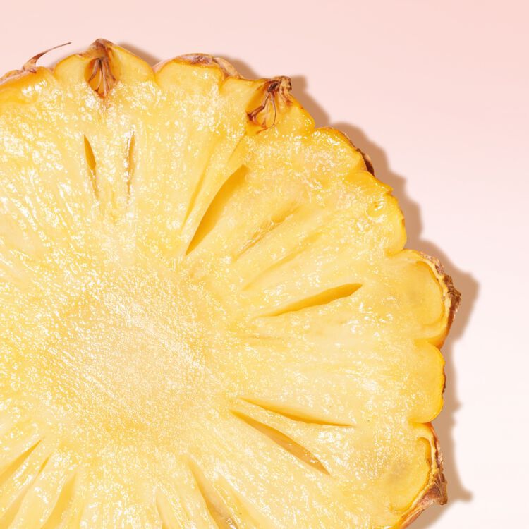 Gros plan sur une tranche d'ananas juteuse et fraiche sur un fond rose pale.