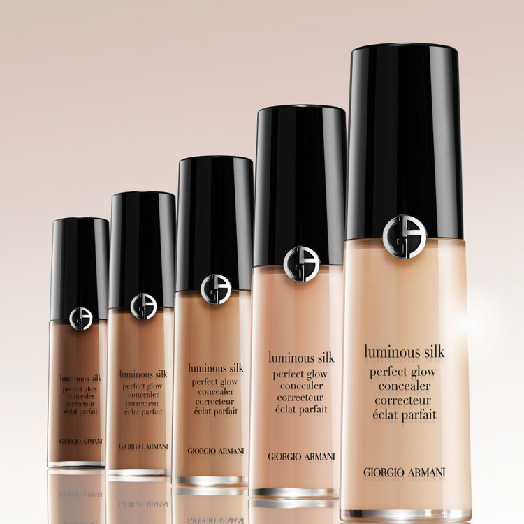 Five bottles of Giorgio Armani Luminous Silk Perfect Glow Concealer arranged in a diagonal row from darkest to lightest shade on a reflective surface against a soft beige background.