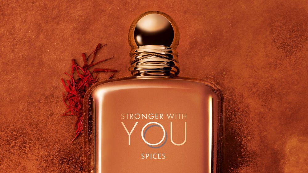 Close-up of ARMANI STRONGER WITH YOU SPICES bottle with gold cap, set against an orange background with saffron and spice accents, showcasing the luxurious and intense scent.