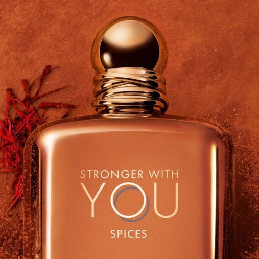Close-up of ARMANI STRONGER WITH YOU SPICES bottle with gold cap, set against an orange background with saffron and spice accents, showcasing the luxurious and intense scent.