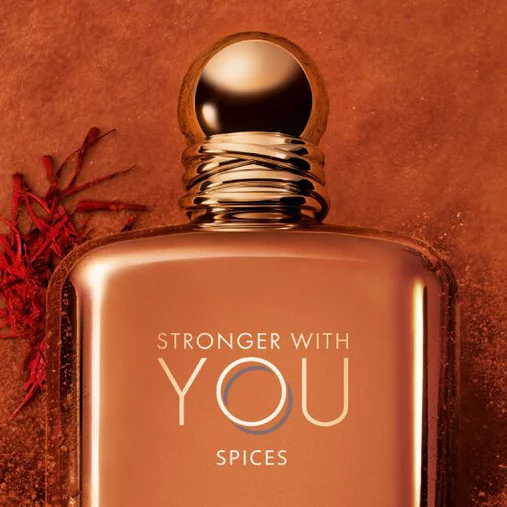 Close-up of ARMANI STRONGER WITH YOU SPICES bottle with gold cap, set against an orange background with saffron and spice accents, showcasing the luxurious and intense scent.