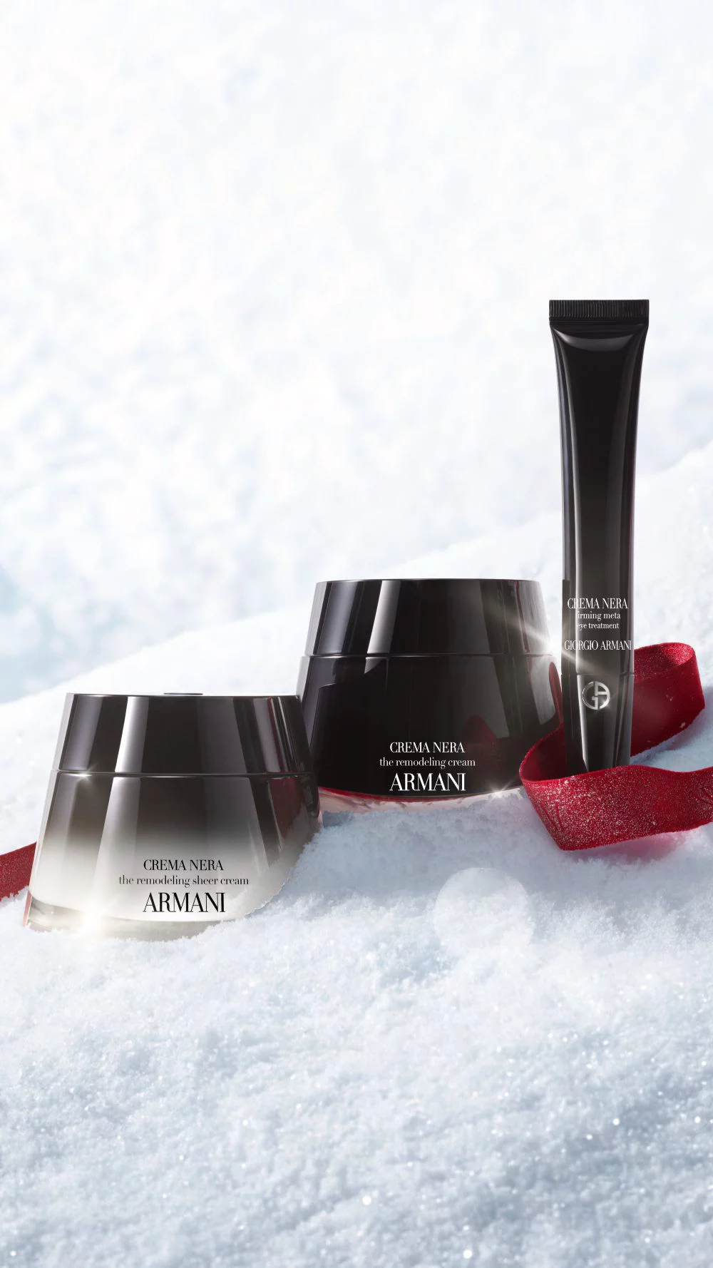 Les produits de soins Armani beauty sur la neige avec un ruban rouge pour le temps des fetes.