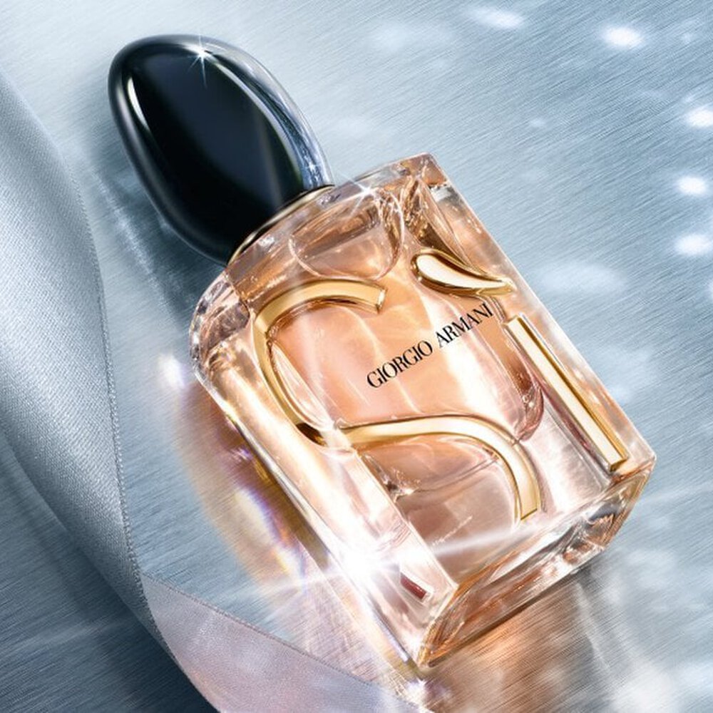 Giorgio Armani Si Eau de Parfum perfume bottles styled on a blue fabric background with sparkling light effects