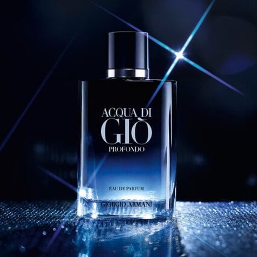 A bottle of Acqua di Gio Profondo Eau de Parfum, featuring a gradient design from a deep black cap and top to a clear, transparent base, stands on a sparkling, reflective surface. Bright starburst highlights reflect off the bottle, and the dark background is softly blurred with blue light accents, enhancing the elegant and intense feel of the fragrance.