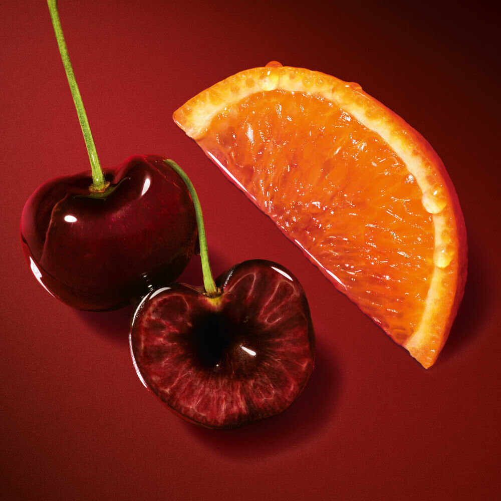 Top Note: fresh cherries and orange slice on a rich red background.