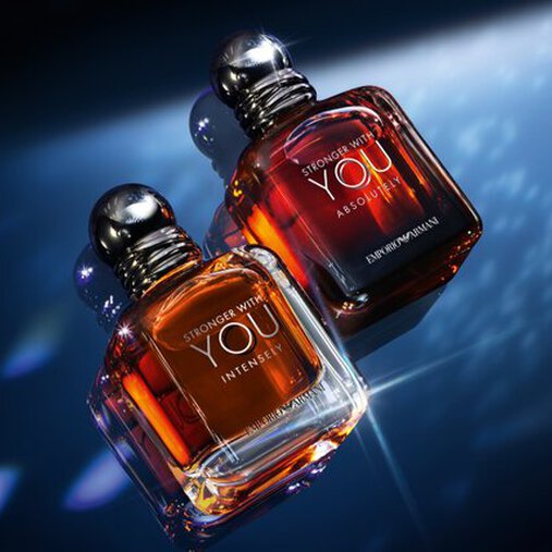 A single bottle of Emporio Armani "Stronger With You Parfum" stands upright on a reflective surface, illuminated by dramatic blue and white lighting against a dark background.
