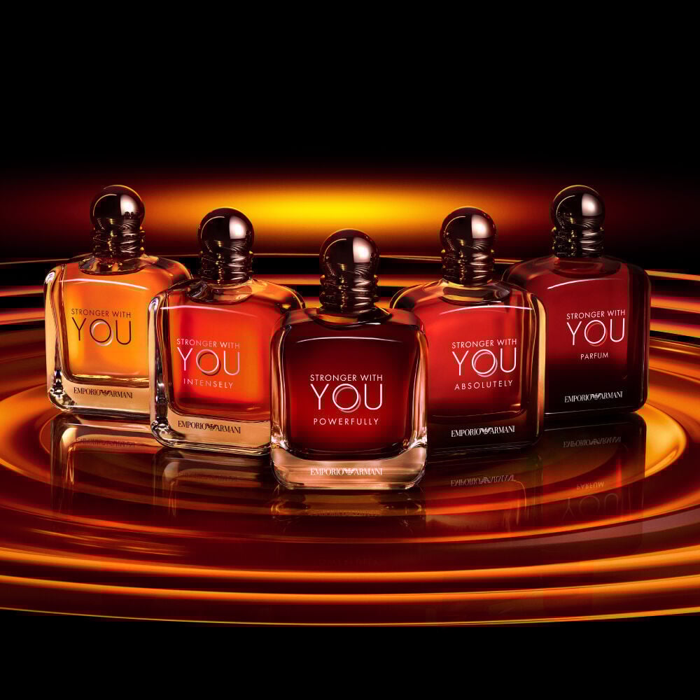Five Armani Stronger With You fragrance bottles, each variant glowing on a radiant, amber-lit background, showcasing the full collection’s bold elegance.