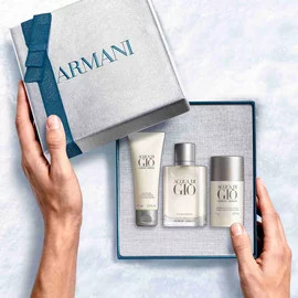 Giorgio Armani Acqua di Gio Eau de Toilette 100ml gift set — hands unveiling the signature bottle, All-Over Body Shampoo 75ml and Deodorant Stick 75g from within the open Armani gift box, an intimate unboxing moment.