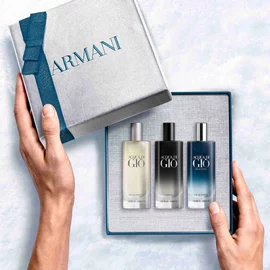 Hands opening a teal-ribboned Armani gift box revealing three Acqua di Gio mini bottles — Eau de Toilette, Profondo Eau de Parfum and Parfum 15ml discovery set.