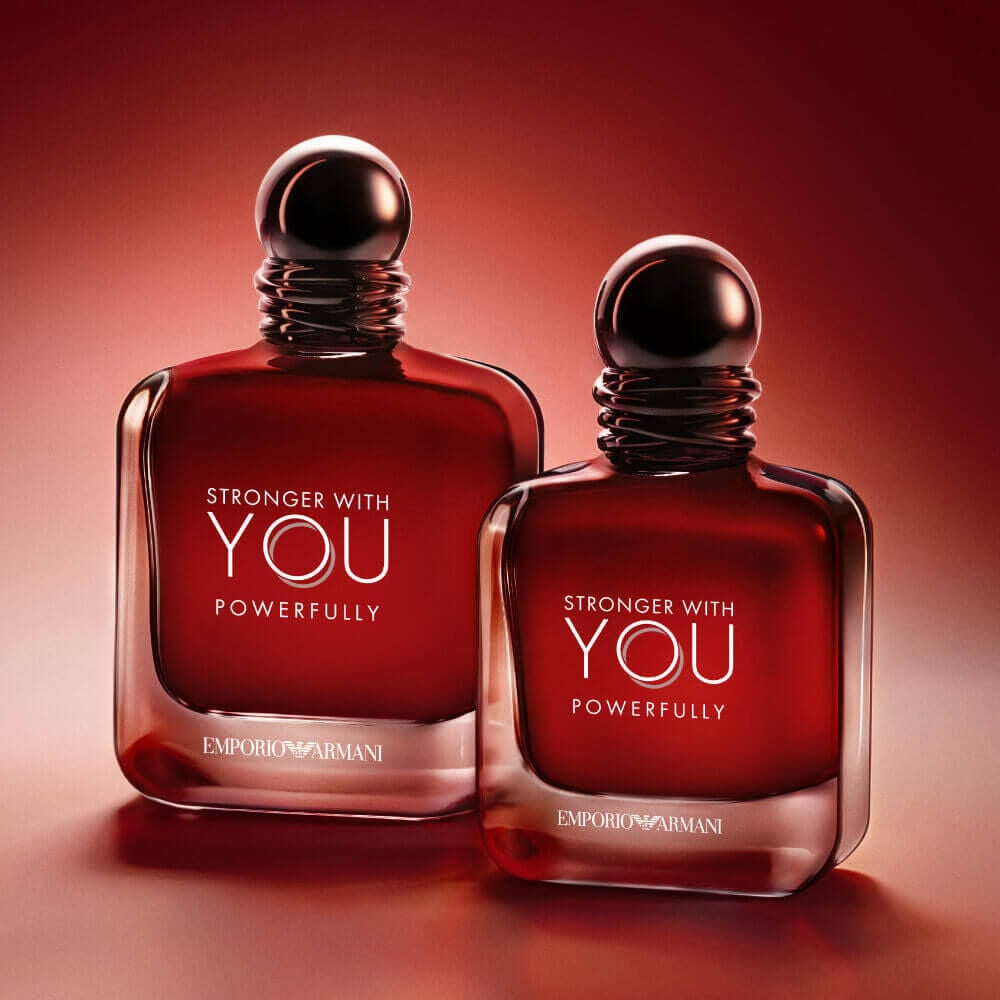 Two Armani Stronger With You Powerfully 50ml and 100ml bottles side by side, glowing on a red backdrop.