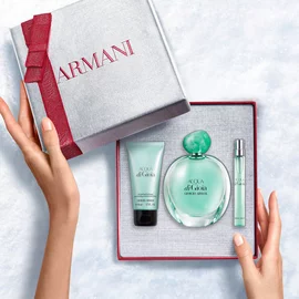 Hands unveiling a red-ribboned white Armani gift box revealing Acqua di Gioia Eau de Parfum 100ml, 10ml and Perfumed Body Lotion 50ml — women's fragrance and body care gift set.