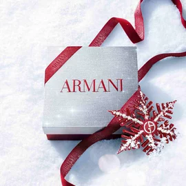 Silver Armani Glamourous Winter Holiday Gift Set box with red glitter ribbon and Giorgio Armani red snowflake ornament resting on a sparkling snowy surface — festive luxury fragrance gift packaging.