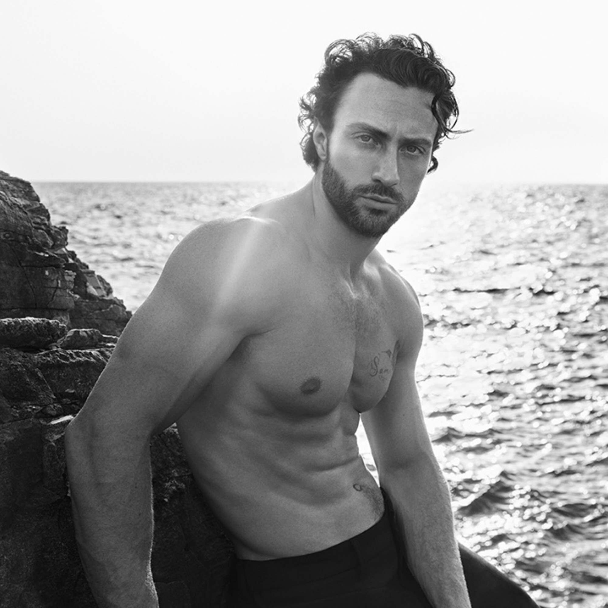 Aaron Taylor-Johnson by the sea, set against a rocky coastline. A black and white marine atmosphere.