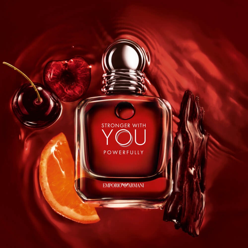 Emporio Armani Stronger With You Powerfully bottle with cherries, orange slice, and wood, on a vibrant red backdrop.